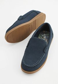 Marineblå ruskinds slip-on sko med gummisål, dekorativ søm og mønstret indersål med grønne botaniske designs.