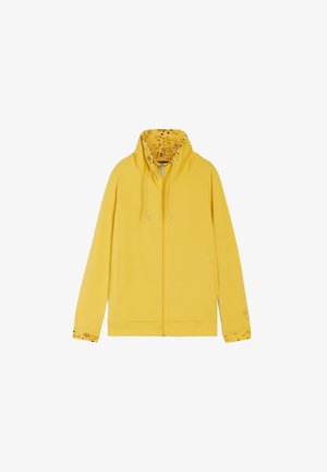 Felpa gialla con zip, con una fodera a stampa floreale nel cappuccio e nei polsini. Presenta delle stringhe e un orlo a coste. Tessuto morbido.