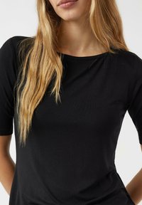 Czarna dopasowana koszulka z krótkim rękawem, wykonana z gładkiej tkaniny. Okrągły dekolt, prosty design oraz elastyczna faktura zapewniająca komfort.