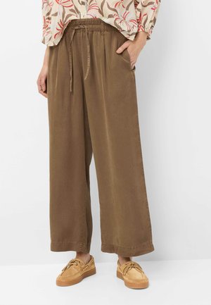 Donna che indossa pantaloni larghi marroni con coulisse in vita, scarpe da barca color beige e una camicetta floreale a maniche lunghe infilata dentro.