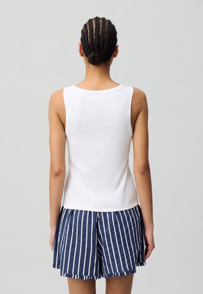 Top sin mangas blanco emparejado con pantalones cortos a rayas en azul marino y blanco, con un corte relajado y una tela suave, con un dobladillo que termina por encima de las caderas.
