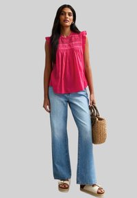 Roze mouwloze top met een gestructureerde halslijn, gecombineerd met lichtblauwe wijde jeans. Accessoires zijn een gevlochten handtas en platform sandalen.