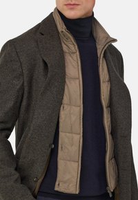 Beżowa, wyściełana kurtka noszona pod ciemnoszarym, teksturowanym żakietem, z granatowym golfem. Widoczne guziki i zamki.