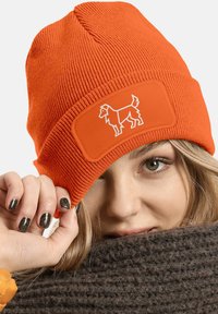 Orange knitted beanie with ribbed texture and a rectangular patch featuring a white dog graphic. Soft material, snug fit.