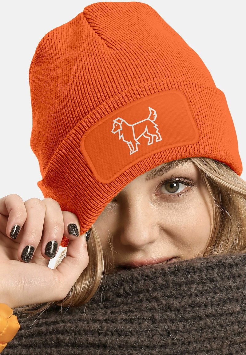 Orange knitted beanie with ribbed texture and a rectangular patch featuring a white dog graphic. Soft material, snug fit.