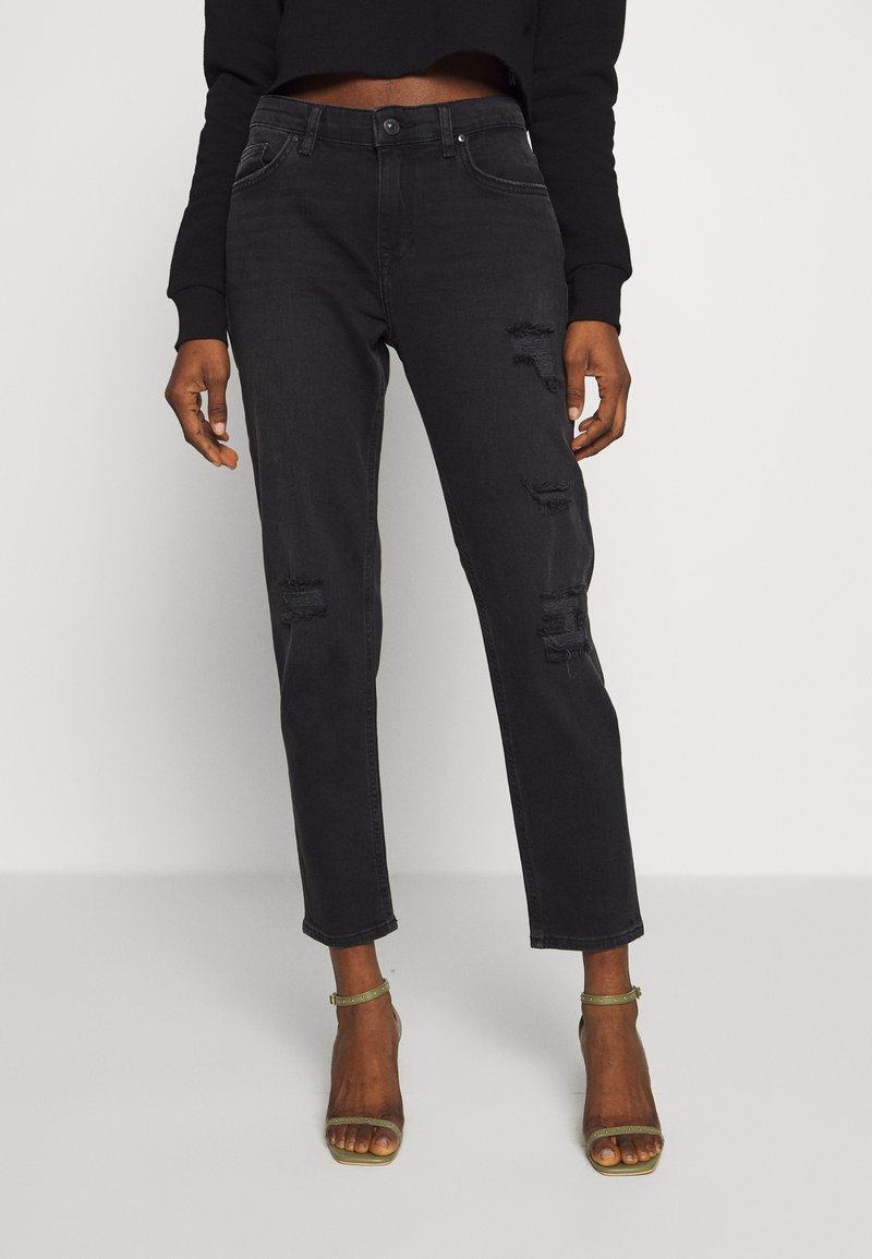 Jeans de mezclilla negra con detalles desgastados, corte recto, cinco bolsillos y cierre de botón, combinados con sandalias doradas con tiras.