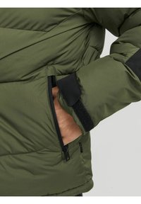 Giacca imbottita verde con cuciture diagonali, una tasca con zip e dettagli in Velcro nero sui polsini per una vestibilità regolabile.