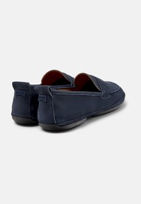 Zapatillas de color azul marino tipo slip-on con parte superior de textil suave, suela de goma e interior de cuero. Presenta un logotipo sutil en el talón.