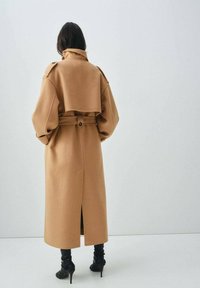 Long, camel-colored coat with a cropped top section, wide sleeves, belted waist, and side slit, made from soft fabric.