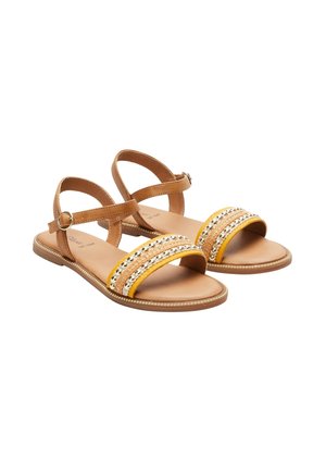 Paire de sandales plates marron avec des brides de cheville et des bandes avant décorées de galon jaune et de perles métalliques.
