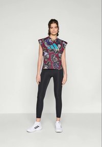 T-shirt graphique à manches courtes, avec un imprimé de papillon vibrant en violet et vert d'eau, associé à un legging noir et des chaussures de sport blanches.