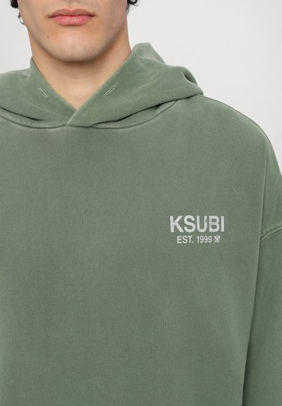 Zielona bluza Ksubi z ribbowanym wykończeniem, z kieszenią typu kangur i haftowanym białym logo na klatce piersiowej. Luźny fason.