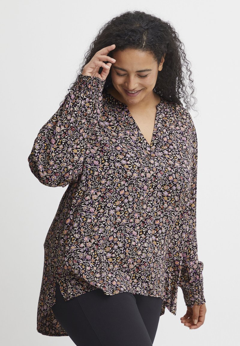 Garums piedurkņu melna blūze ar ziedu rakstu rozā un dzeltenā krāsā, ar V-veida izgriezumu, brīvu piegriezumu un sānu šķēlumiem gaisa plūsmai.