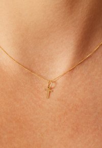 Gold necklace with a fine chain featuring a small, polished cross pendant. The texture is smooth, with a shiny finish.