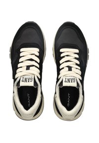 Černé tenisky s bílými tkaničkami, které kombinují hladké a strukturované materiály, zaoblenou špičku a polstrovaný interiér. Viditelné jméno značky.