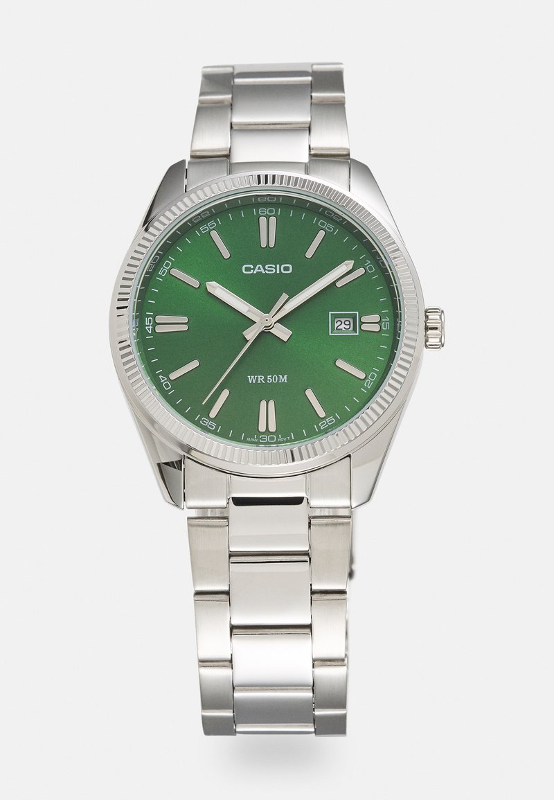 Montre en acier inoxydable argenté avec un cadran rond vert, index horaires argentés, affichage de la date et bracelet en maillon métallique. Résistante à l'eau jusqu'à 50 mètres.