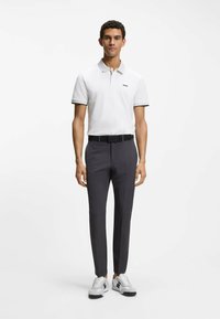 Camiseta polo blanca con cuello y detalles grises, combinada con pantalones ajustados de color gris oscuro y zapatillas blancas con detalles en negro.