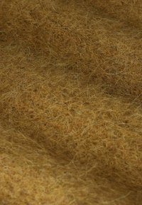 Nahaufnahme eines weichen, flauschigen, senfgelben Fabriks mit feinen, lockigen Fasern und einer strukturierten Oberfläche.