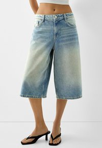 Ljust blå denim culotter med en blekt finish, rak benmodell, hög midja och rå nederkant. Tillsammans med svarta flip-flops.