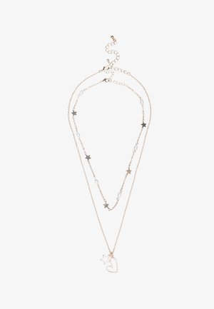 Collier superposé comprenant trois chaînes : métal doré avec des accents en étoile, perles argentées et un pendentif en forme de cœur. Fermoir ajustable.