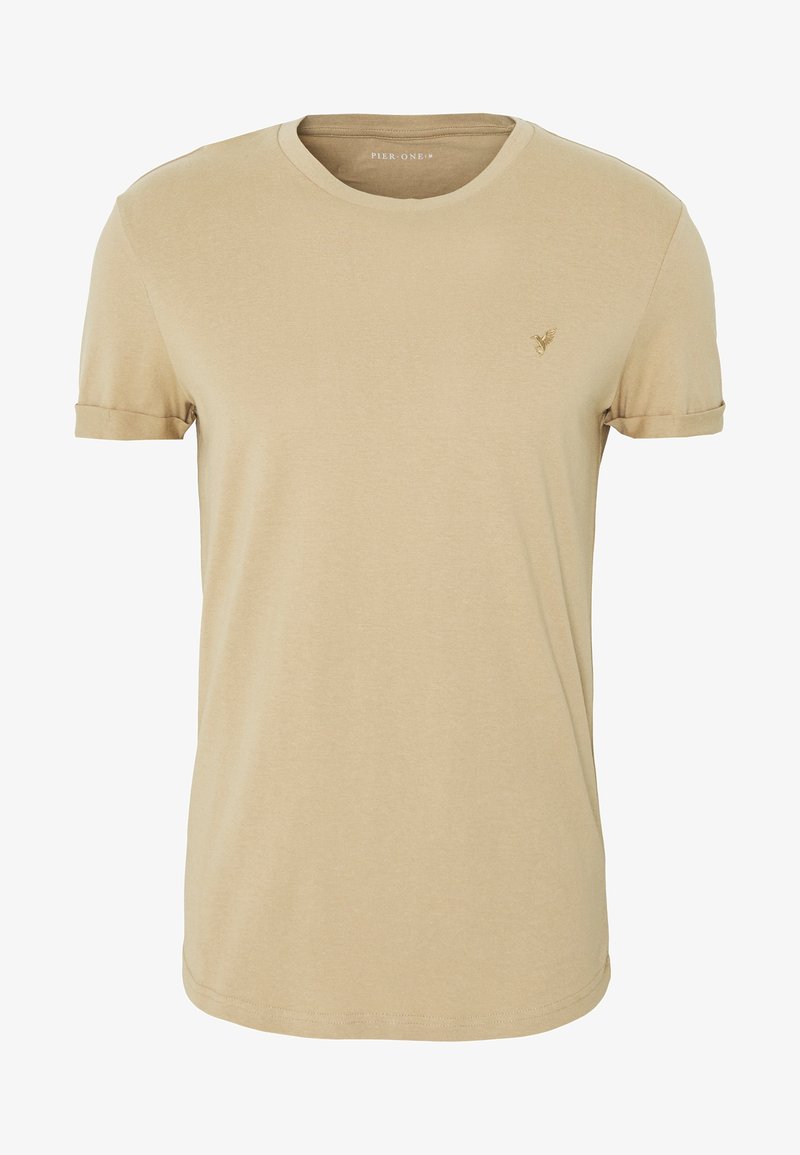 T-shirt beige à manches courtes et col rond avec petit logo brodé sur la poitrine gauche et revers de manches retroussés.