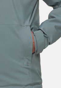 Lysblå, mat stofjakke med en skjult lomme, justerbare manchetter og et slankt, minimalistisk design. Syningerne er synlige.