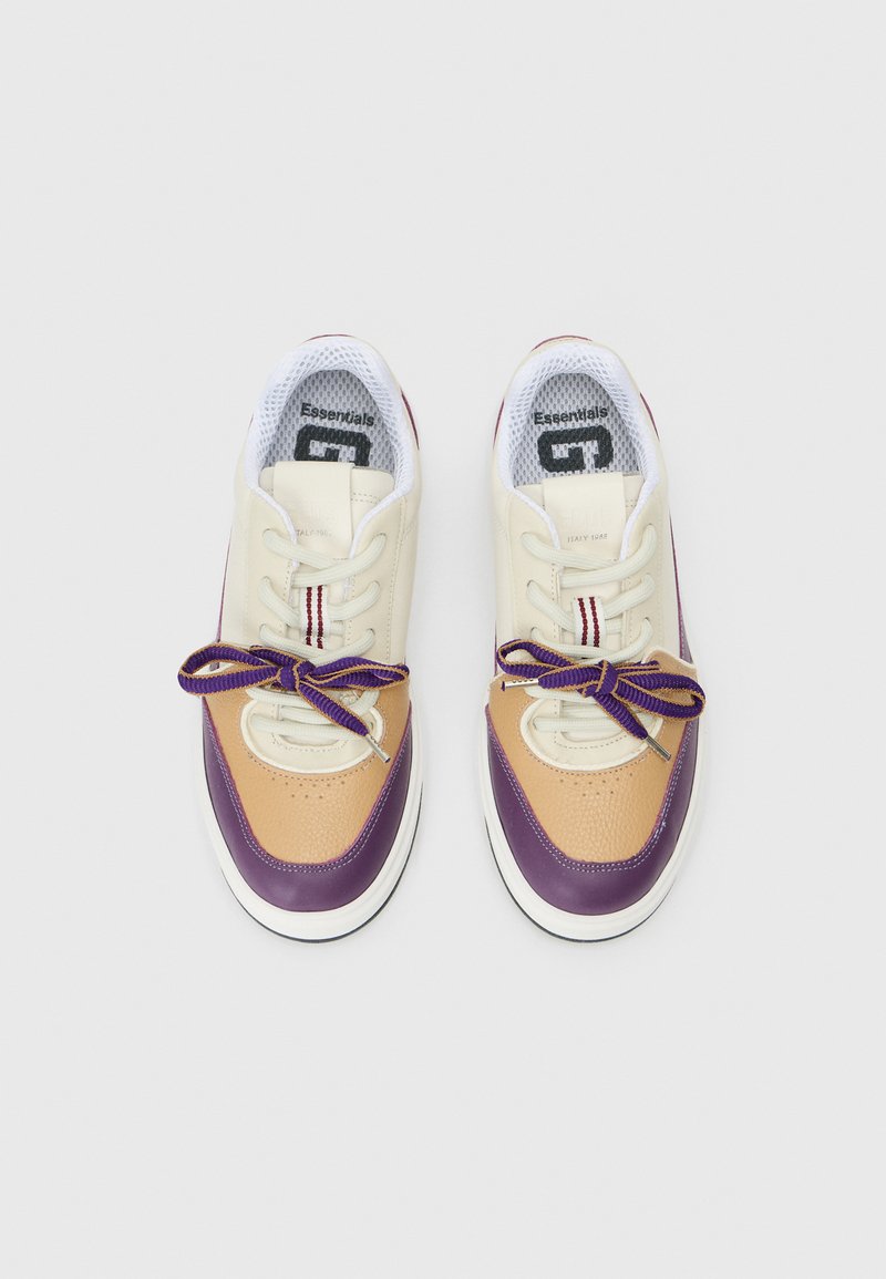 Baskets avec une tige en cuir beige et des accents violets et beige. Bout rond, semelle blanche et lacets violets. Doublure en maille visible.