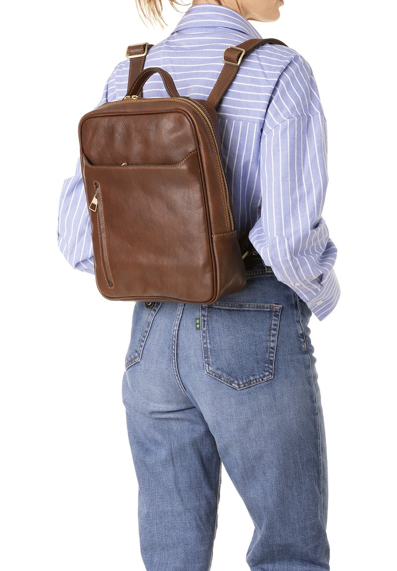 Sac à dos en cuir marron de forme rectangulaire, avec fermeture éclair et poche avant. Texture lisse, bretelles réglables et détails de couture subtils.