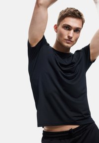 Sort kortærmet atletisk t-shirt med en afslappet pasform, glat tekstur og diskret vandret linje-detaljering på forsiden.