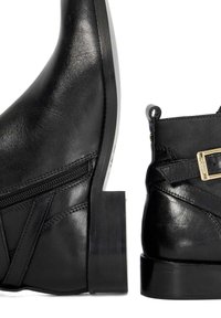 Bottines en cuir noir avec fermeture éclair sur le côté, une texture lisse, des coutures décoratives et un petit talon bloc orné d'une boucle métallique.