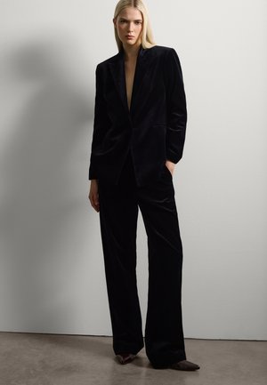 Schwarze Samtjacke und -hose im Slim Fit, mit schmalen Revers und Seitentaschen. Glatte Textur mit einem dezenten Glanz.