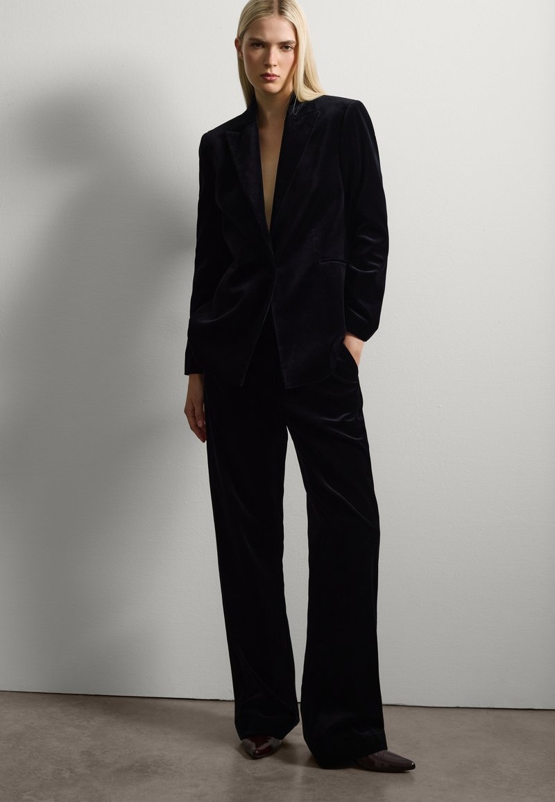 Schwarze Samtjacke und -hose im Slim Fit, mit schmalen Revers und Seitentaschen. Glatte Textur mit einem dezenten Glanz.