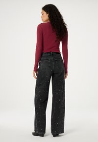 Dunkelgraue, weit geschnittene Jeans mit Perlenverzierungen, hoher Taille, fünf Taschen und textured Oberfläche, kombiniert mit einem eng anliegenden, burgunderfarbenen Rippenoberteil.