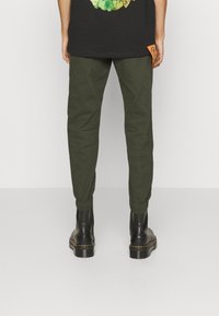 Groene katoenen joggers met elastische boorden, met een zichtbare oranje tag op de achterzak, gecombineerd met zwarte enkellaarzen.