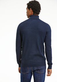 Marineblauer Rollkragenpullover aus einem weichen Strickstoff mit langen Ärmeln und einer taillierten Passform, kombiniert mit dunklen Denim-Jeans.