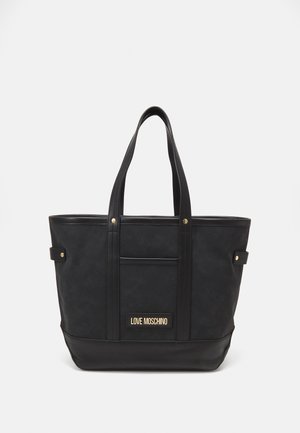 Zwarte Moschino totebag met dubbele handvatten, voorvak met applicatie en goudkleurige hardware op een effen lichte achtergrond.