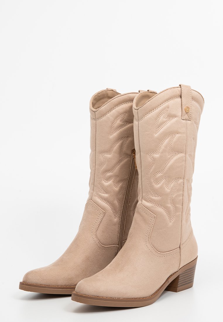 Botas de cowboy de ante sintético beige con puntera afilada, detalles de costura, cremallera lateral y tacón apilado para mayor altura y estabilidad.