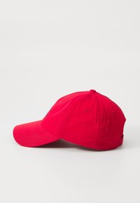 Punainen puuvillainen baseball-lippis, jossa on kaareva lippa, säädettävä hihna takana ja brodeerattu logo etupaneelissa.