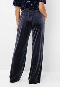 Pantalon large en velours bleu marine avec taille élastique, présentant une texture lisse et une coupe décontractée, s'étendant jusqu'au sol.
