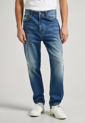 Light blue denim jeans with a relaxed fit, featuring faded areas and distressed detailing. Paired with white sneakers.