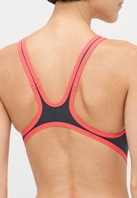 Soutien-gorge de sport avec un corps bleu foncé et des bretelles et bordures corail contrastantes, conçu dans un style dos nageur pour un soutien et une flexibilité.