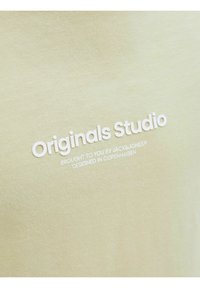 Šviesiai žalia marškinėlių su užrašu "Originals Studio" baltu tekstu. Lygus, minkštas audinys su pritaikytu kirpimu. Paprastas dizainas, be matomų raštų.