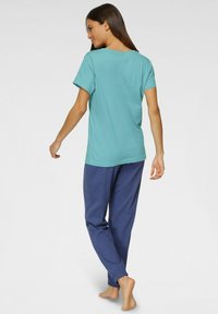 Turquoise cotton T-shirt with short sleeves paired with navy blue jogger pants with elastic cuffs, shown from a backward angle.