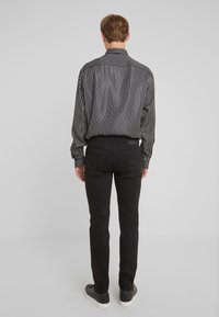 Camisa de rayas blancas y negras con un cuello tradicional, combinada con pantalones ajustados negros y zapatillas negras, vista desde la parte de atrás.