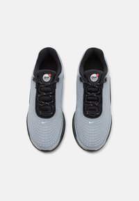 Zapatillas deportivas grises con parte superior de malla texturizada, cierre de cordones negros y suela de goma; presentan un logotipo circular en la lengüeta.