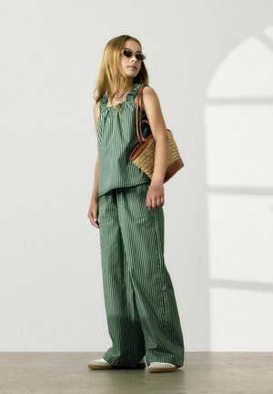 Haut sans manches rayé vert et blanc avec un décolleté froncé, associé à un pantalon large assorti. Accessoirisé avec un sac tissé.