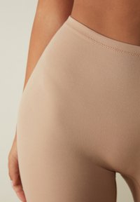 Beige high-waisted legging met een soepel textuur, voorzien van een platte tailleband en subtiele stiksels langs de randen.