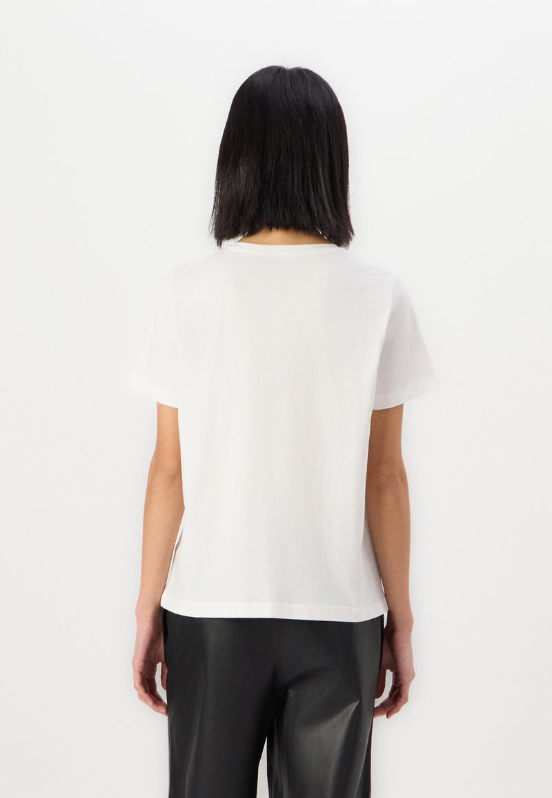 T-shirt en coton blanc à manches courtes, col rond et coupe décontractée, associé à un pantalon léger noir.