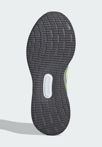 Suela de zapato con una parte inferior de goma negra texturizada, que presenta una ranura central y acentos blancos. La sección superior muestra detalles en verde y gris.