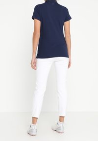 Marinblå polo med korta ärmar, kombinerad med åtsittande vita byxor och grå sportskor. Slätt tyg med klassisk krage.